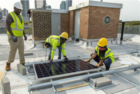 Photo of three construction workers installing a solar panel on an NYC rooftop