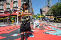 Photo of a woman roping off a section of street containing a freshly painted mural of abstract animals.