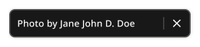 The open component is a wide black rectangle with white text. The example reads "Photo by Jane John. D. Doe" On the right side of the container there is a vertical bar and a white "X" icon.
