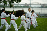 Photo of young people in karate gis practicing martial arts in a park with a bridge in the background.