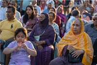Photo of people of South Asian descent sitting outside taking in an event.