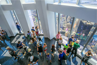 Overhead photo of many people socializing in a high-rise. Manhattan buildings can be seen out of tall windows. 