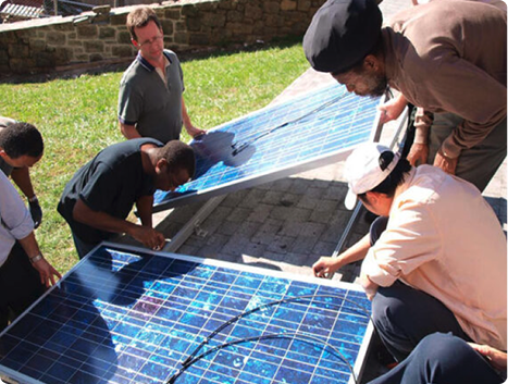 Candid photo of six people installing solar panels on a rooftop.
