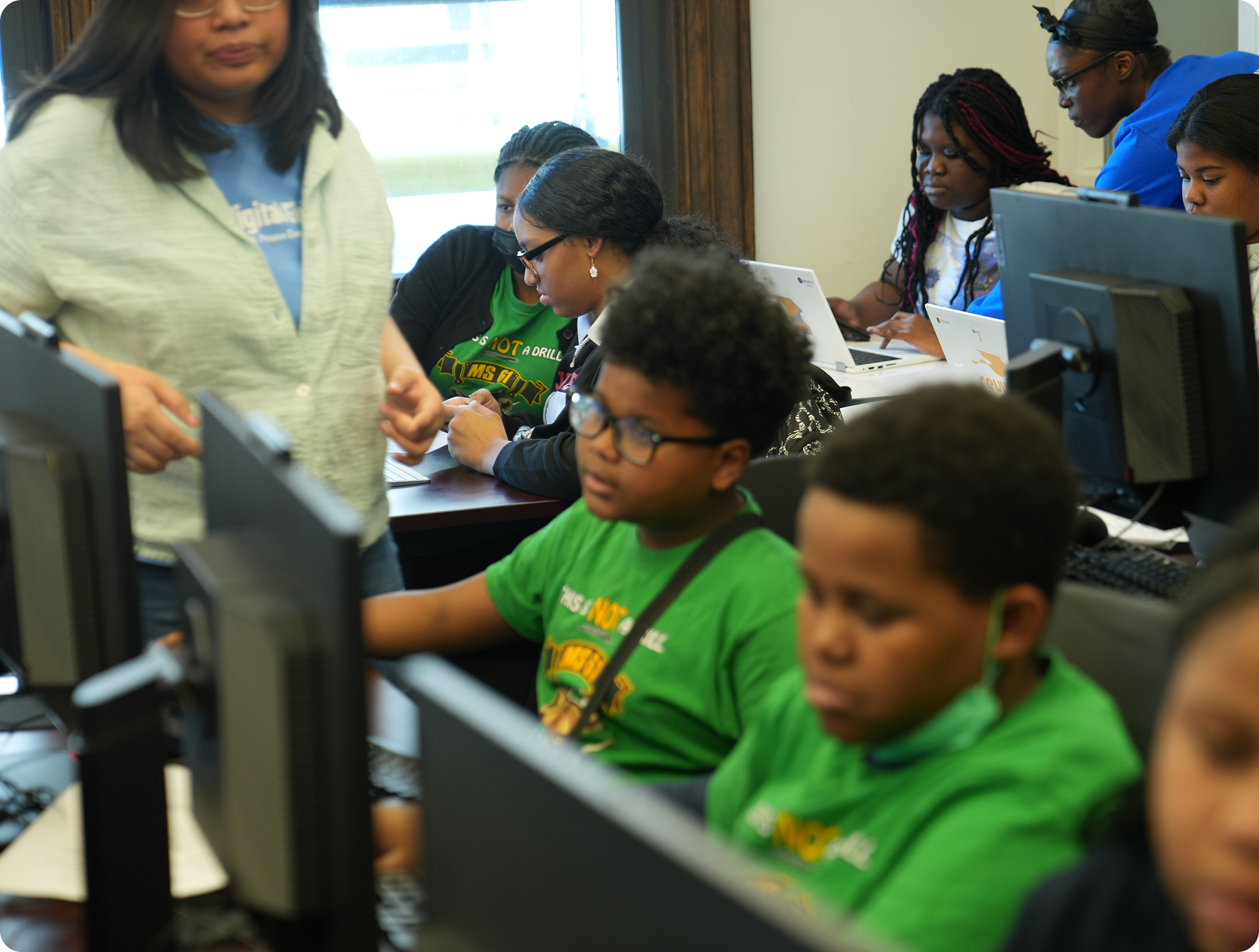 Photo of children using desktop computers in a computer lab as adults supervise